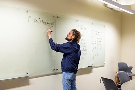 Man in a classroom writes on a whiteboard.