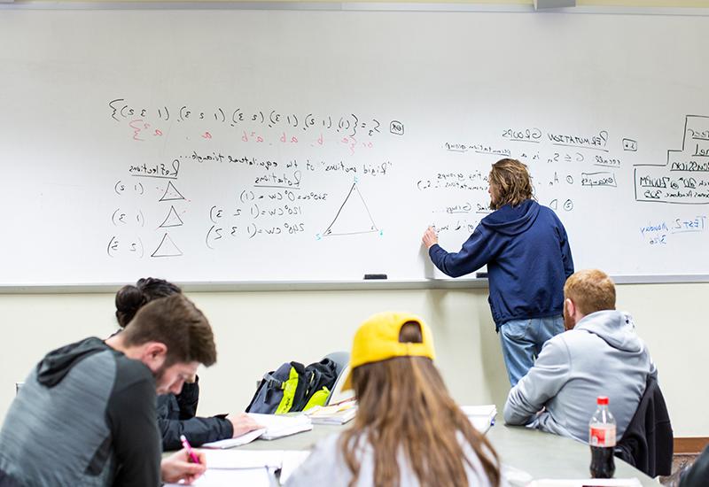 A professor writes on a whiteboard while four students take notes.