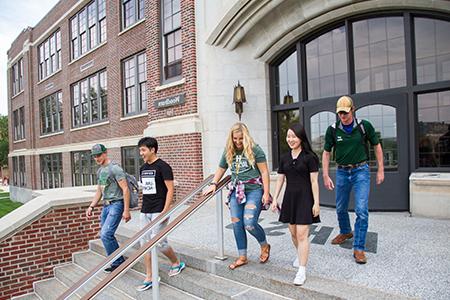 Five students walk down the stairs outside Woodburn Hall.